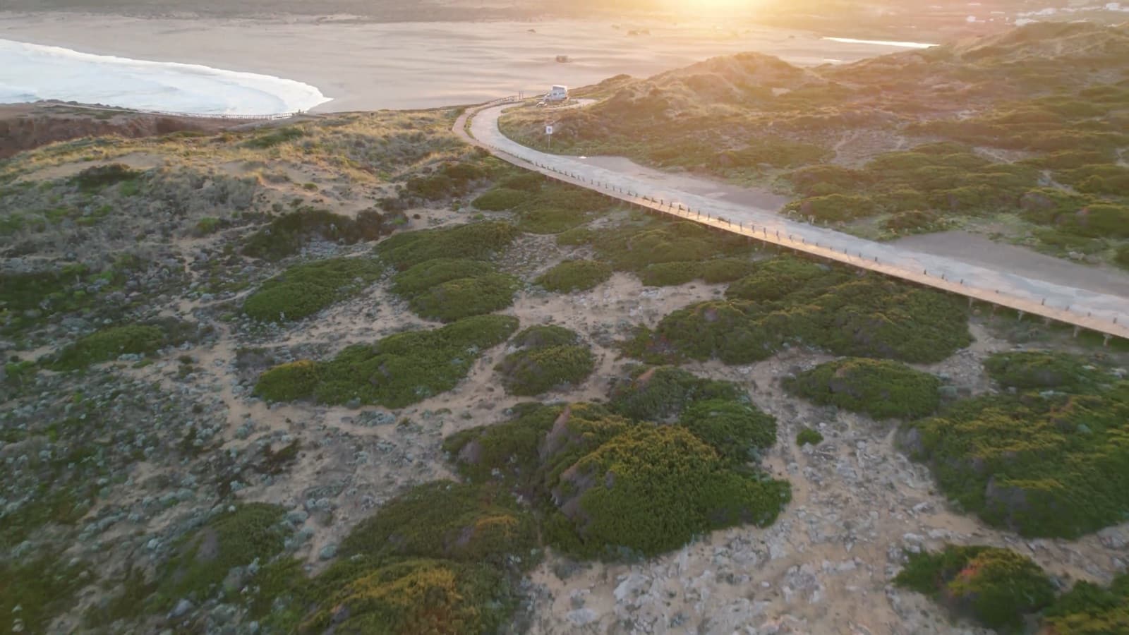 Luchtbeeld van een camper op een duinweg langs de kust bij zonsondergang